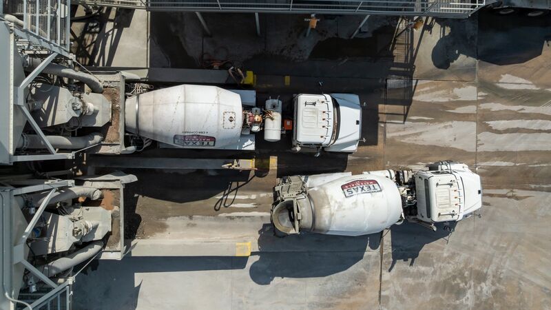 Mixer trucks loading under the batch plant silos — straight-down aerial